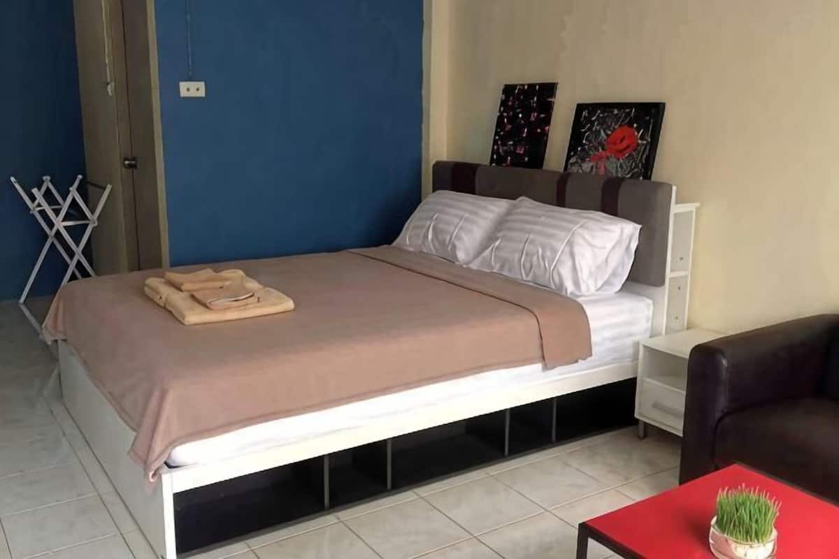 Un lit avec une couverture, une table de chevet, une chaise et une petite table sur laquelle est posée une plante.