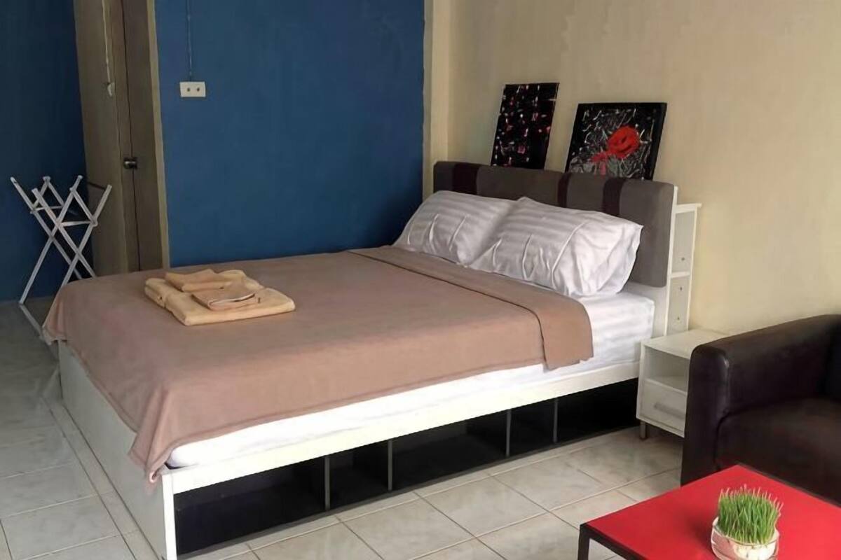 A bed with a blanket, a nightstand, a chair, and a small table with a plant.