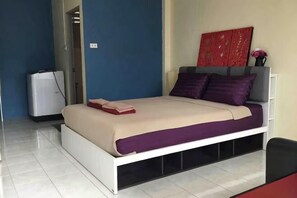 Una cama con estructura blanca, colcha roja y beige, y almohadas moradas.