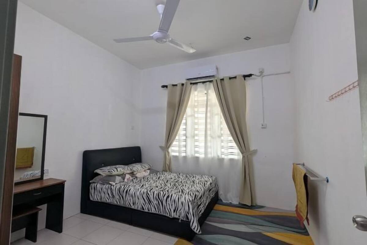 A bedroom with a bed, a desk, a ceiling fan, and a window with curtains.