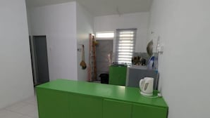 A small kitchen with a green countertop, a kettle, and a window with blinds. - Homestay ibunda (Sabak Bernam)