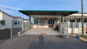 A gated parking area with a covered entrance, a motorcycle, and a building with a green roof. - Homestay ibunda (Sabak Bernam)