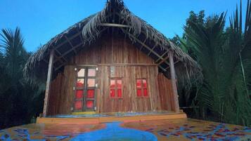 A wooden house with a thatched roof, large windows, and a colorful floor design.