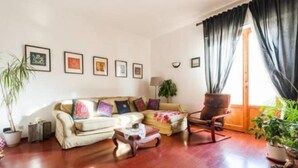 A living room with a sofa, armchairs, a coffee table, and a large window with curtains. - erike balcony (Florence)