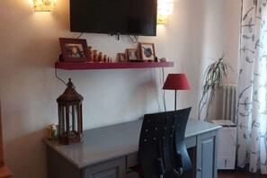 A room with a desk, a chair, a television mounted on the wall, a red lamp, and a plant. - erike balcony (Florence)