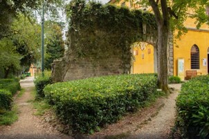 Un sendero que lleva a un edificio amarillo con un muro de piedra y un árbol que se extiende sobre él.