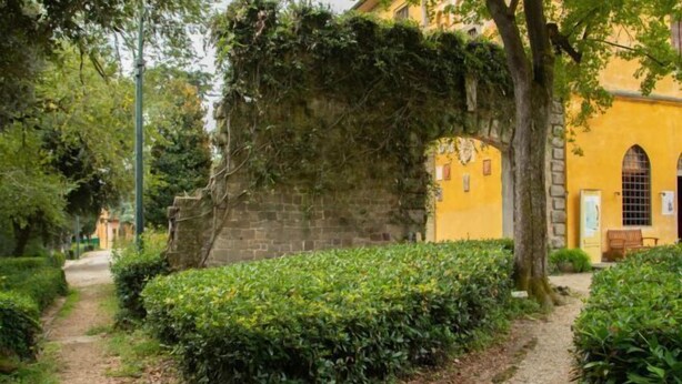 A pathway leading to a yellow building with stone walls and arched windows. - erike balcony (Florence)
