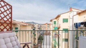 A balcony with a cushioned chair, a lattice structure, and a view of a residential area with buildings and a mountain in the background. - erike balcony (Florence)