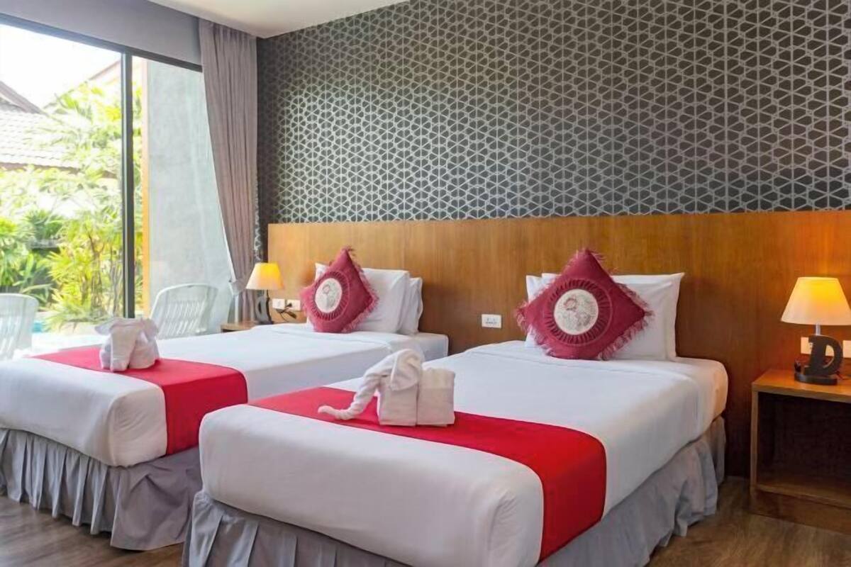 Habitación de hotel con dos camas, cada una con colcha roja y almohadas blancas, cabeceros de madera y pared estampada.