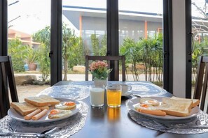 A table set with breakfast items including toast, sausage, and eggs, with a view of greenery and a building in the background. - Oho Luxury Pool Access (Phuket)
