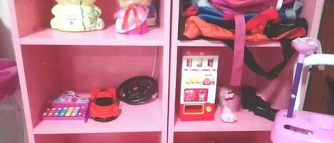 A pink shelf with various children's toys and items, including a toy car, a toy guitar, and a toy train.