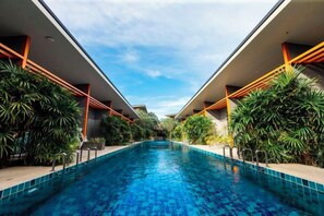 Une piscine aux bords rectilignes, entourée de verdure et bordée d’une architecture moderne.