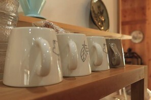 Une rangée de tasses en céramique blanche, ornées de motifs originaux, est posée sur une étagère en bois.