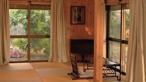 Ein Zimmer mit Tatami-Matten, einem Fernseher und großen Fenstern mit Vorhängen.