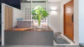 Un espacio exterior moderno con un banco de madera, una planta en maceta y una pared blanca con un diseño geométrico.