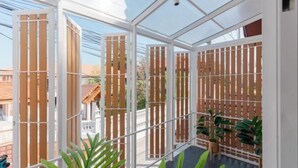 Un balcón con cerramiento de vidrio, listones verticales de madera y plantas en macetas.