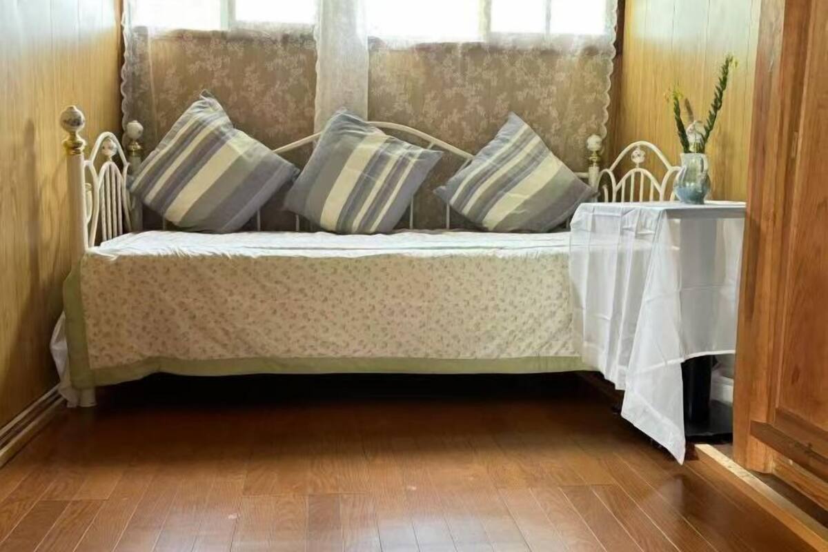 A single bed with a floral bedspread, striped pillows, and a small table with a vase.