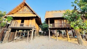 Deux maisons en bois aux toits de chaume, dotées de balcons en bois et entourées d’un sol en gravier.