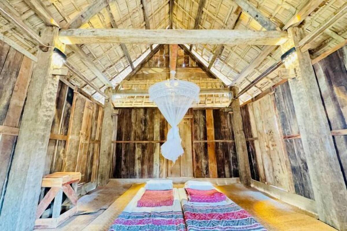 A rustic wooden room with a high ceiling and a hanging light fixture. There are two beds with patterned bedding.