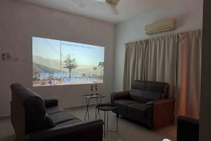 A living room with a large screen, two sofas, a small table, and a ceiling fan.