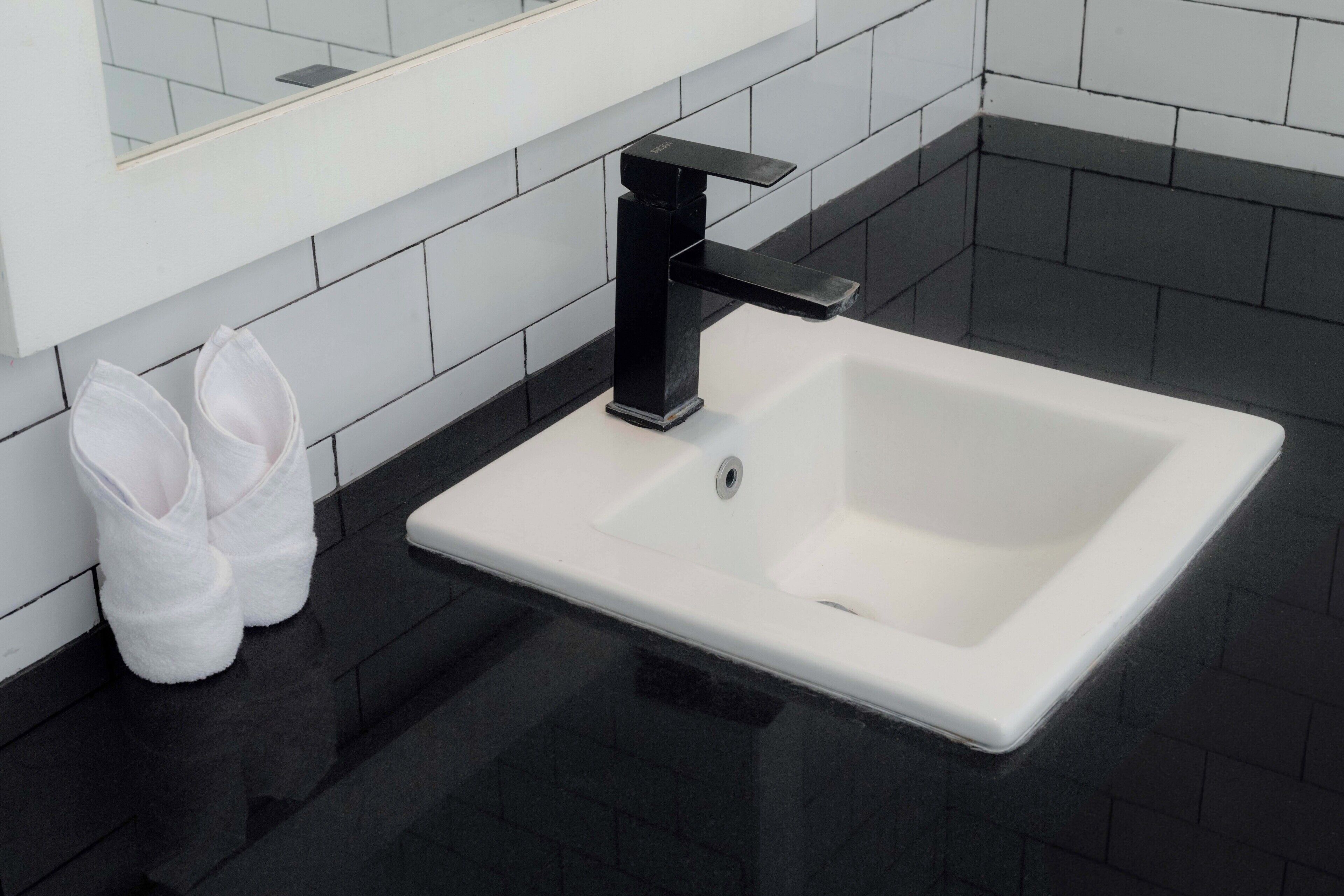 A bathroom with a white sink, black faucet, and white towels on the floor.