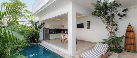 Un espacio exterior moderno con piscina, terraza de madera y una silla de descanso.