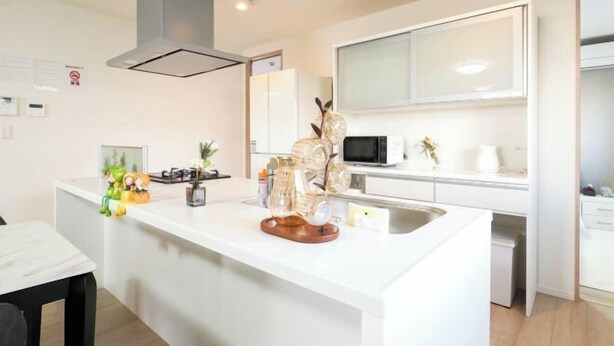 A modern kitchen with a central island, white cabinetry, a microwave, and a stainless steel sink. - youmeiyado asahi matu 3F (Osaka)