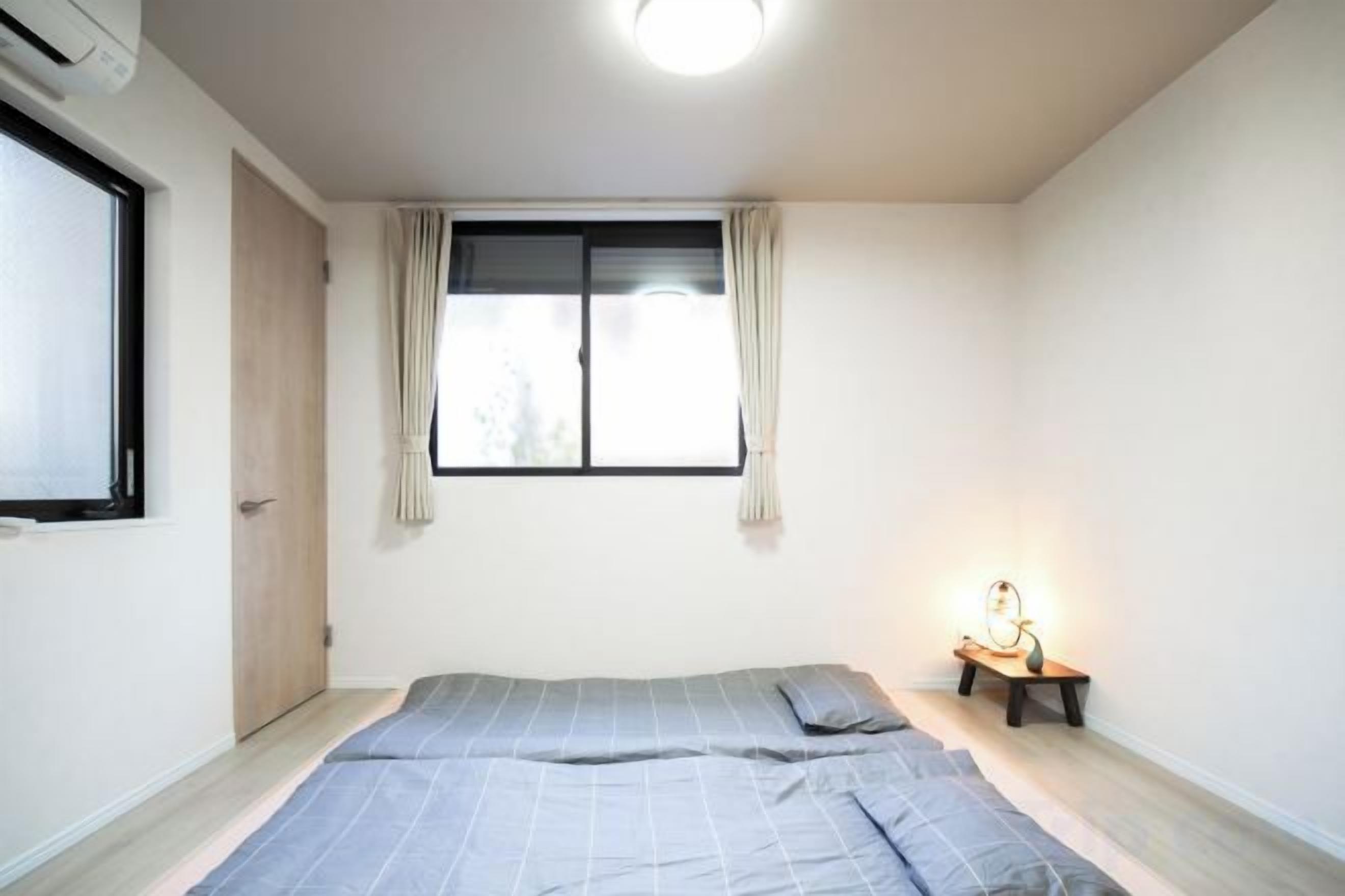 Quarto com cama, mesa de cabeceira, janela com cortinas e ar condicionado fixado na parede.