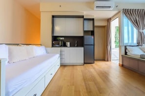 Une chambre d’hôtel compacte comprenant un lit, une kitchenette et une porte coulissante donnant sur un balcon.