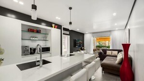 A modern kitchen with a central island, a dining area with bar stools, a sofa, and a large red vase.