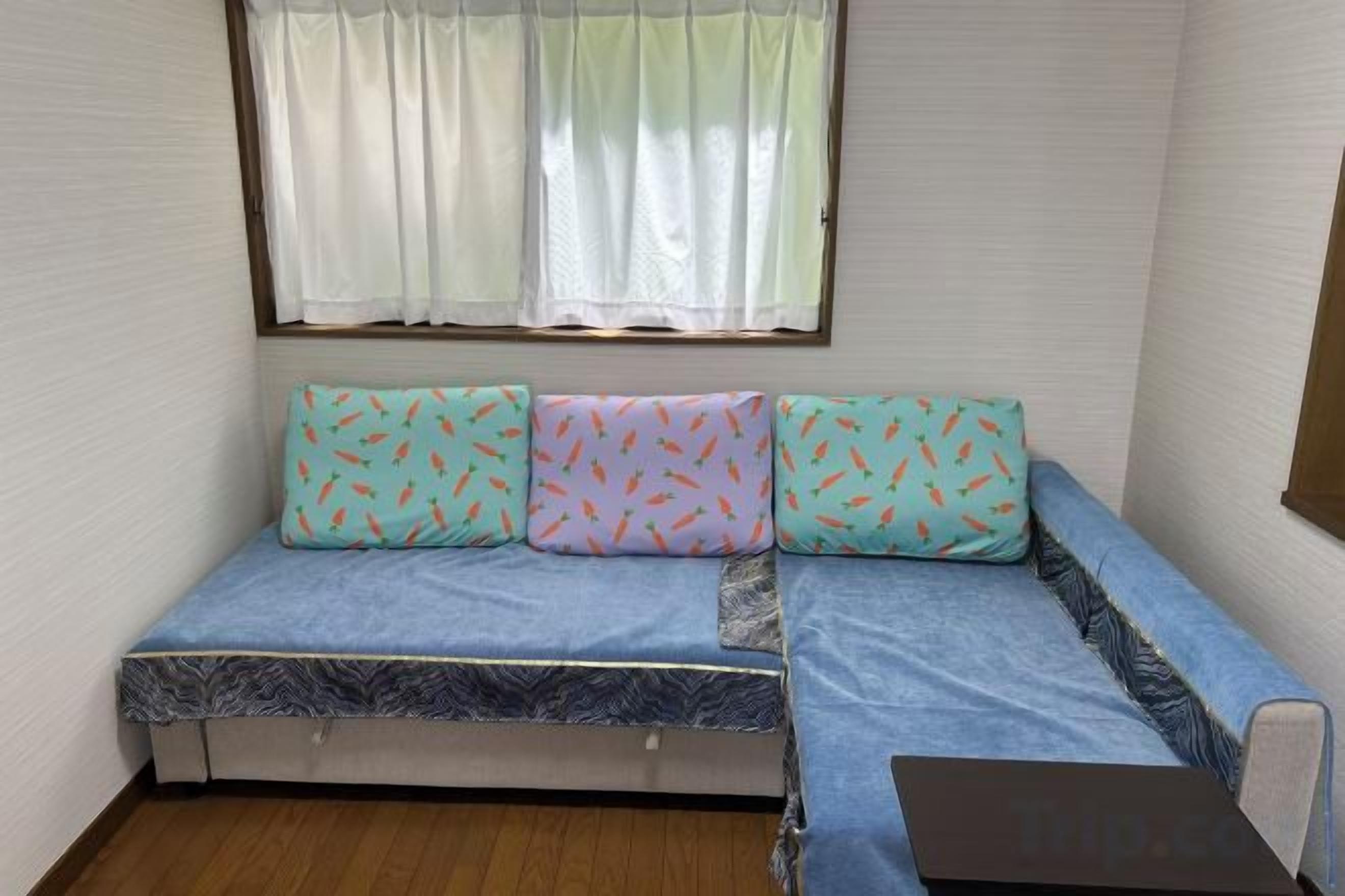 A compact room with a sofa bed, a small table, and a window with curtains.