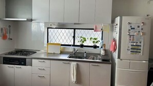A kitchen with white cabinets, a stove, a sink, and a refrigerator. - Flower Tea Hotel (Tokyo)