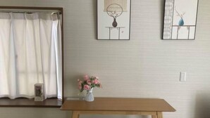 A room with a wooden table, two grey chairs, a white vase with pink flowers, and a window with white curtains. - Flower Tea Hotel (Tokyo)