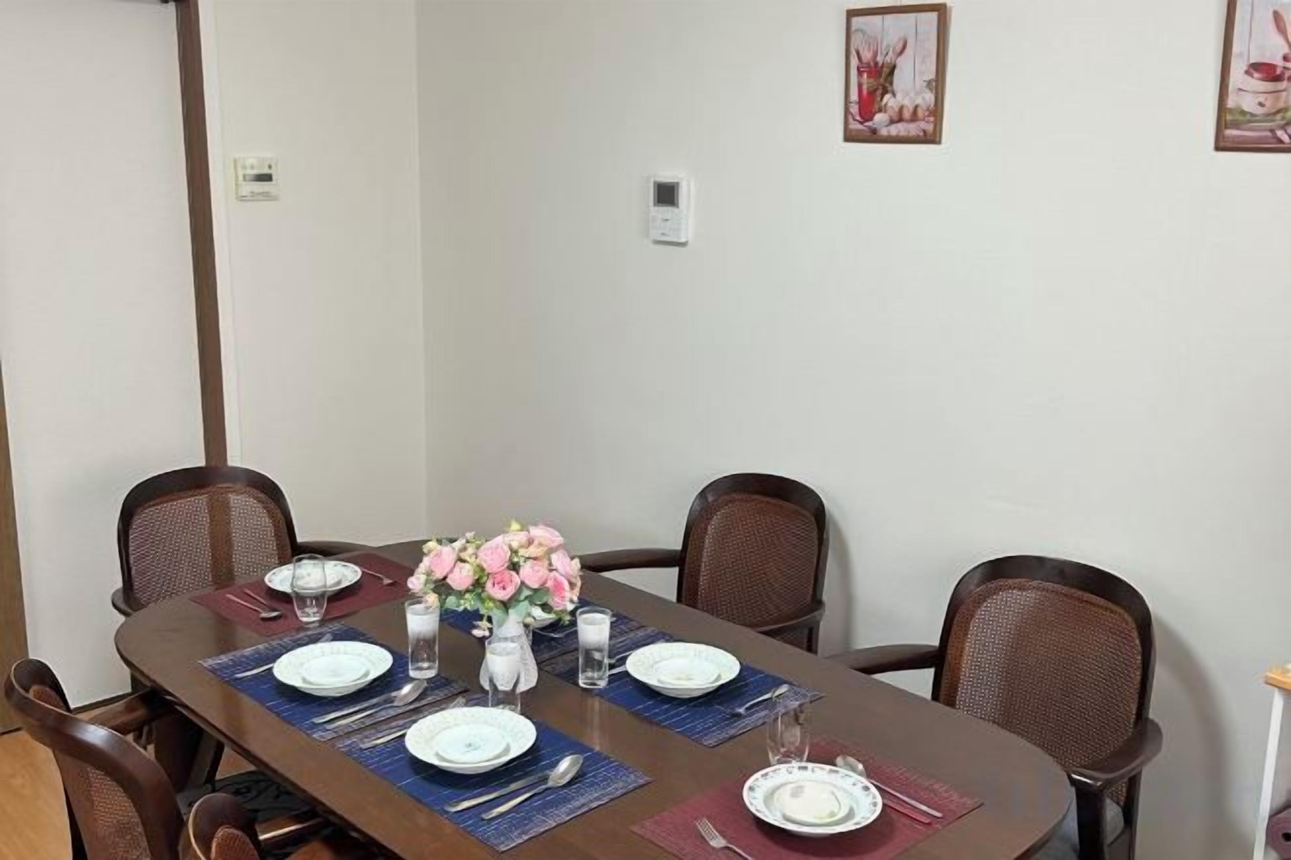 A dining table set for four with chairs, a vase of flowers, and a wall-mounted thermostat.