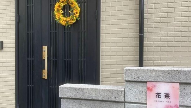 A black door with a yellow floral wreath, a stone bench, and a sign that reads "flower tea". - Flower Tea Hotel (Tokyo)