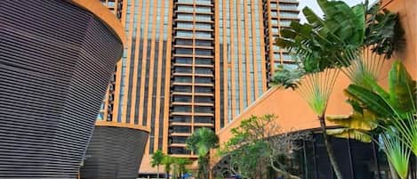 A hotel with a swimming pool, a tall building in the background, and a curved structure to the left.