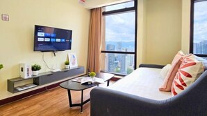 A modern hotel room with a large bed, a flat-screen TV mounted on the wall, a small desk with a plant, and a window offering a city view. - Berjaya Times Square 1BR Suite 5Pax Bukit Bintang Steps to Monorail (Kuala Lumpur)