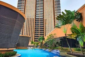 A modern hotel with a swimming pool, surrounded by lush greenery and tall buildings. - Berjaya Times Square 1BR Suite 5Pax Bukit Bintang Steps to Monorail (Kuala Lumpur)