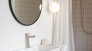 Een moderne badkamer met een witte wastafel, een ronde spiegel en een douchehoek.