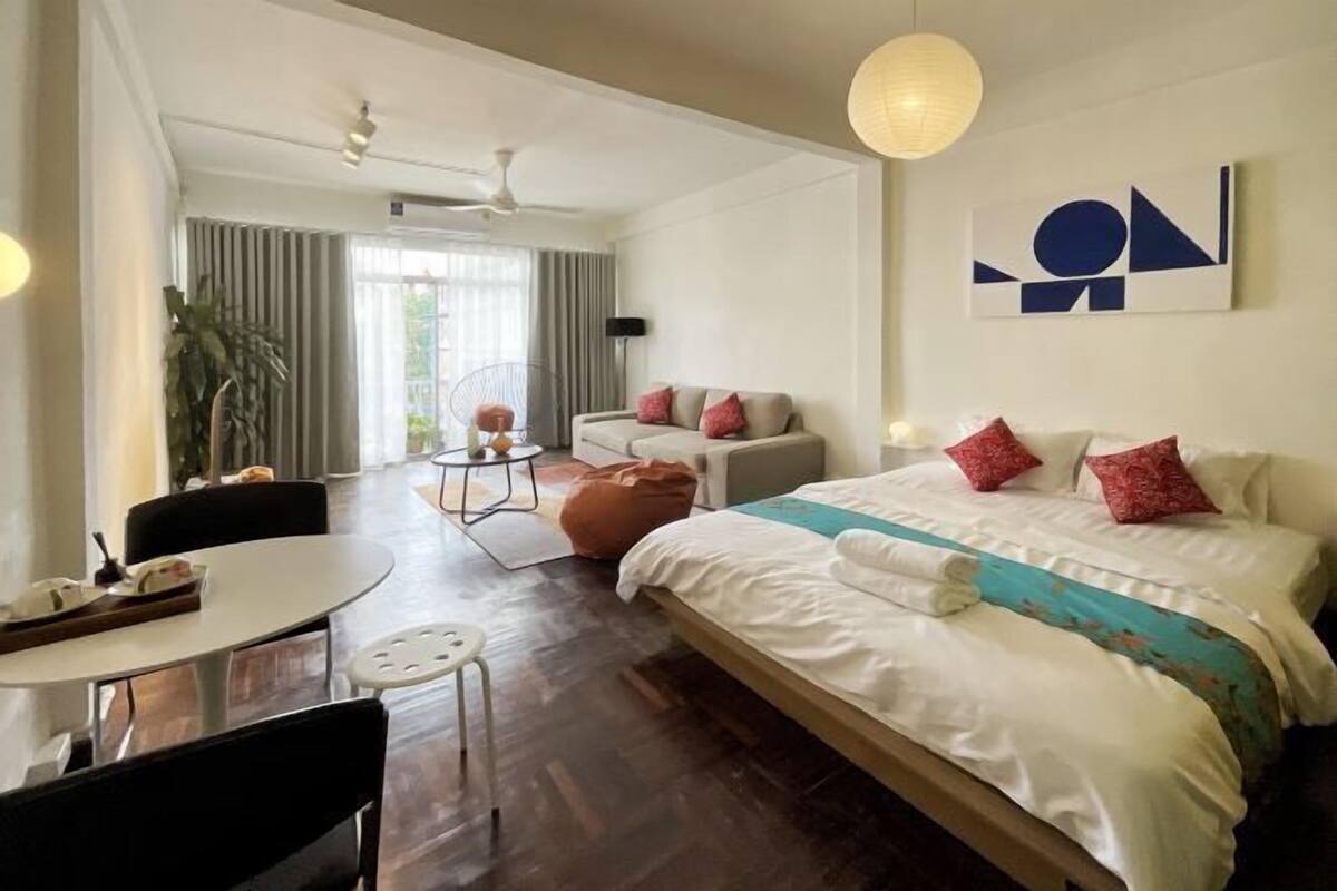 A hotel room with a large bed, a sofa, a dining table, and a ceiling fan.