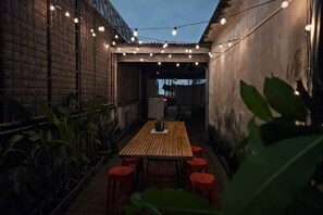 A patio with a wooden table and red stools, surrounded by potted plants and string lights. - SANT BANGKOK (Bangkok)