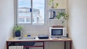 Een kleine keuken met raam, een magnetron, een waterkoker en een spoelbak.