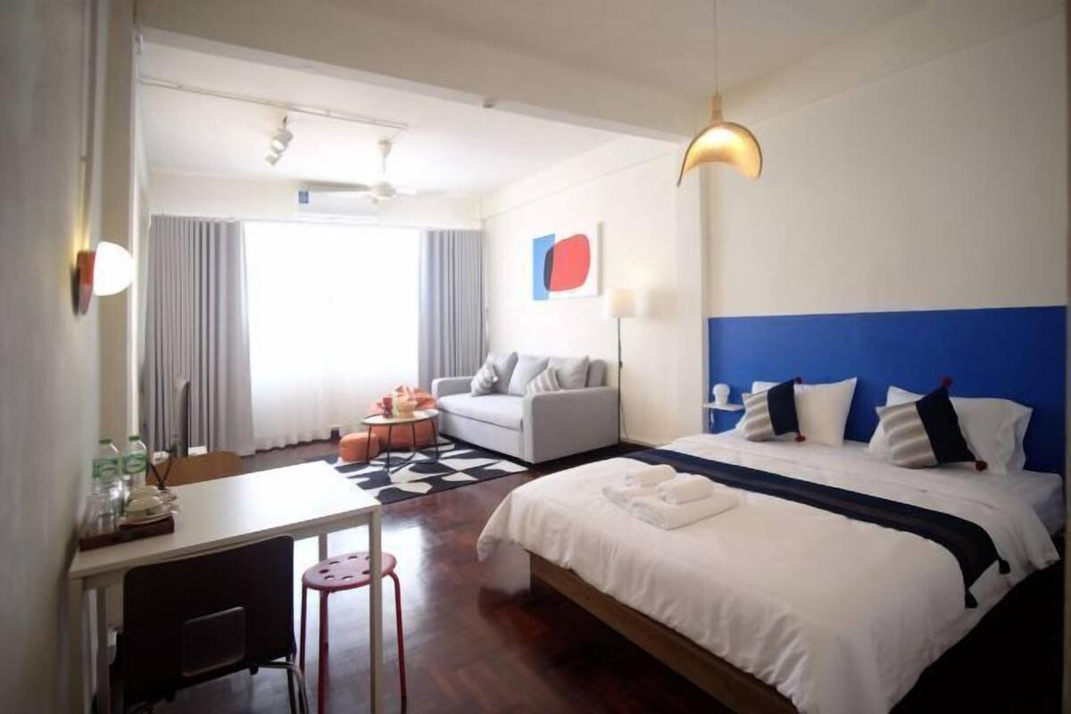 A hotel room with a bed, a desk, a chair, a sofa, and a dining table.