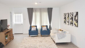 A modern living room with a white sofa, two blue armchairs, a large rug, and abstract wall art.