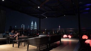 An outdoor seating area with wicker furniture, a view of the city skyline, and illuminated spherical decorations. - Expressionz#KLCC#1BR#Skypool#NEW (Kuala Lumpur)