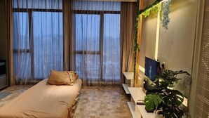 A bedroom with a bed, a desk, a chair, and a large window with curtains. - Expressionz#KLCC#1BR#Skypool#NEW (Kuala Lumpur)