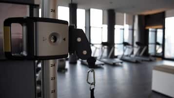 A gym with exercise equipment, including treadmills and a weight machine, with large windows in the background.