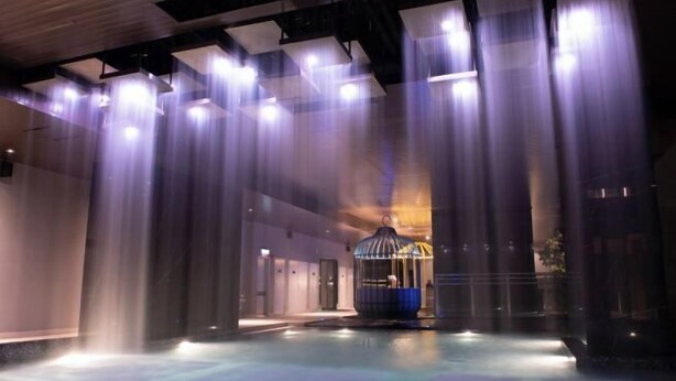 A modern interior with a central water feature, a glass enclosure, and a ceiling with linear light fixtures. - Expressionz#KLCC#1BR#Skypool#NEW (Kuala Lumpur)