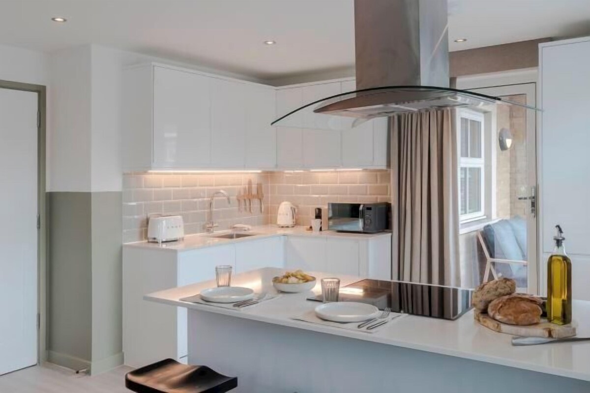 A modern kitchen with white cabinetry, a glass island, and a stainless steel range hood.
