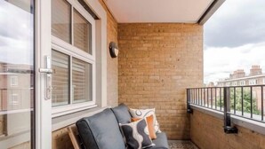Een balkon met een bakstenen muur, een glazen deur en een metalen hekwerk.